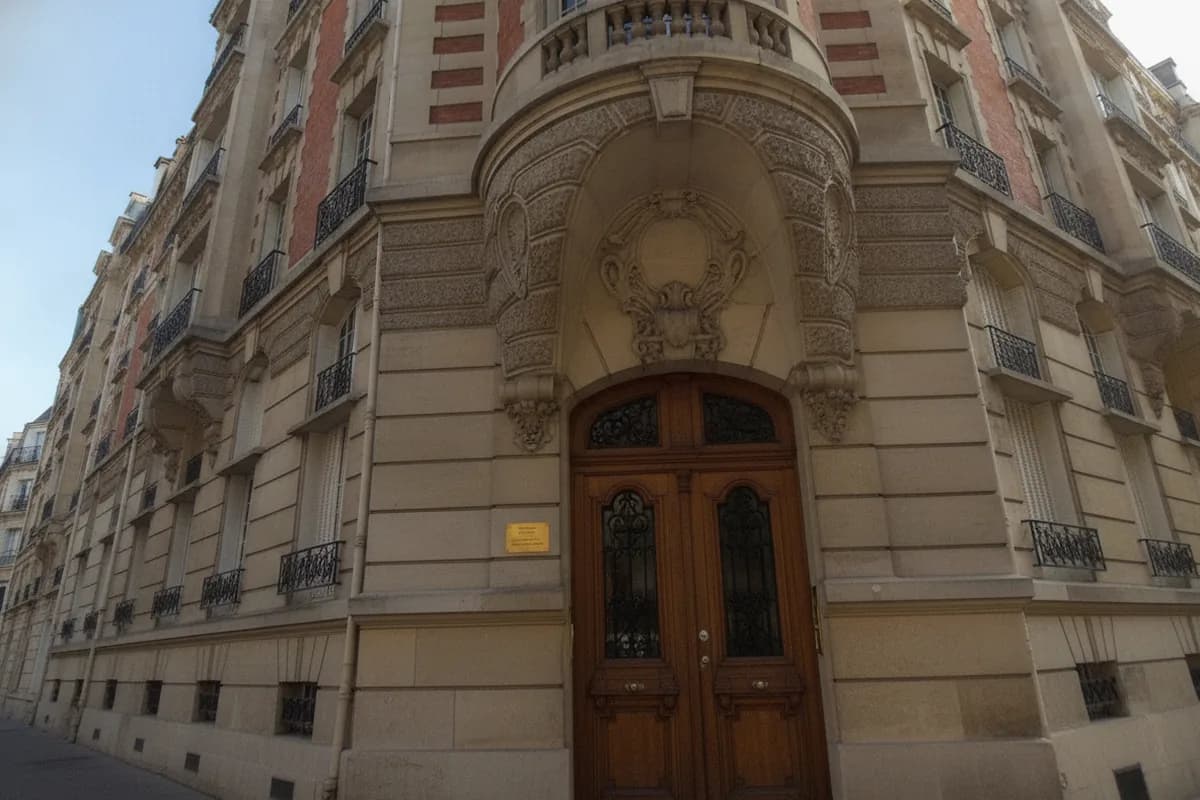 Porte cochère en bois sous un porche sculpté, à l’angle d’un immeuble parisien en pierre et brique